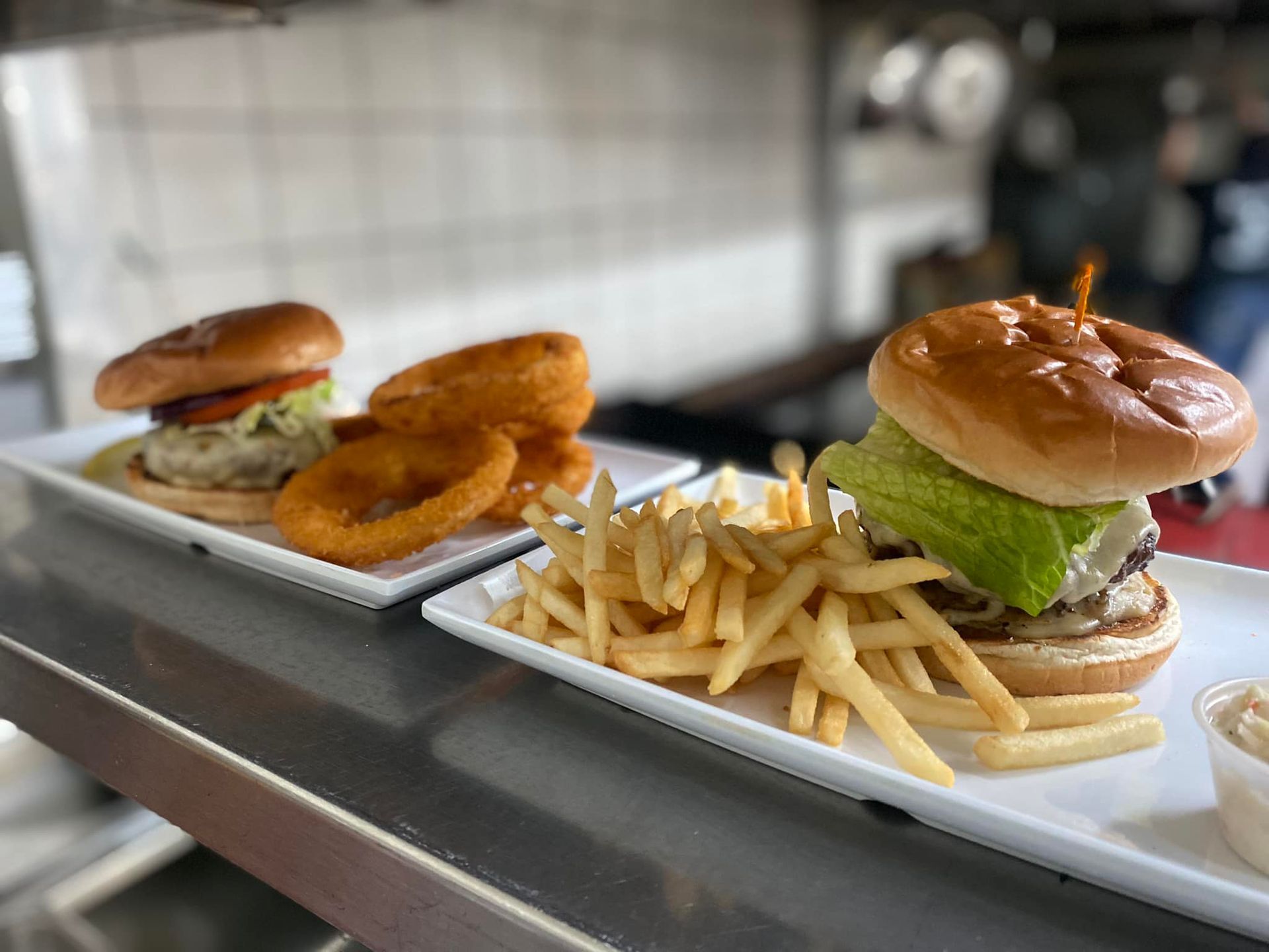 Two burgers with fries and onion rings on white plates.