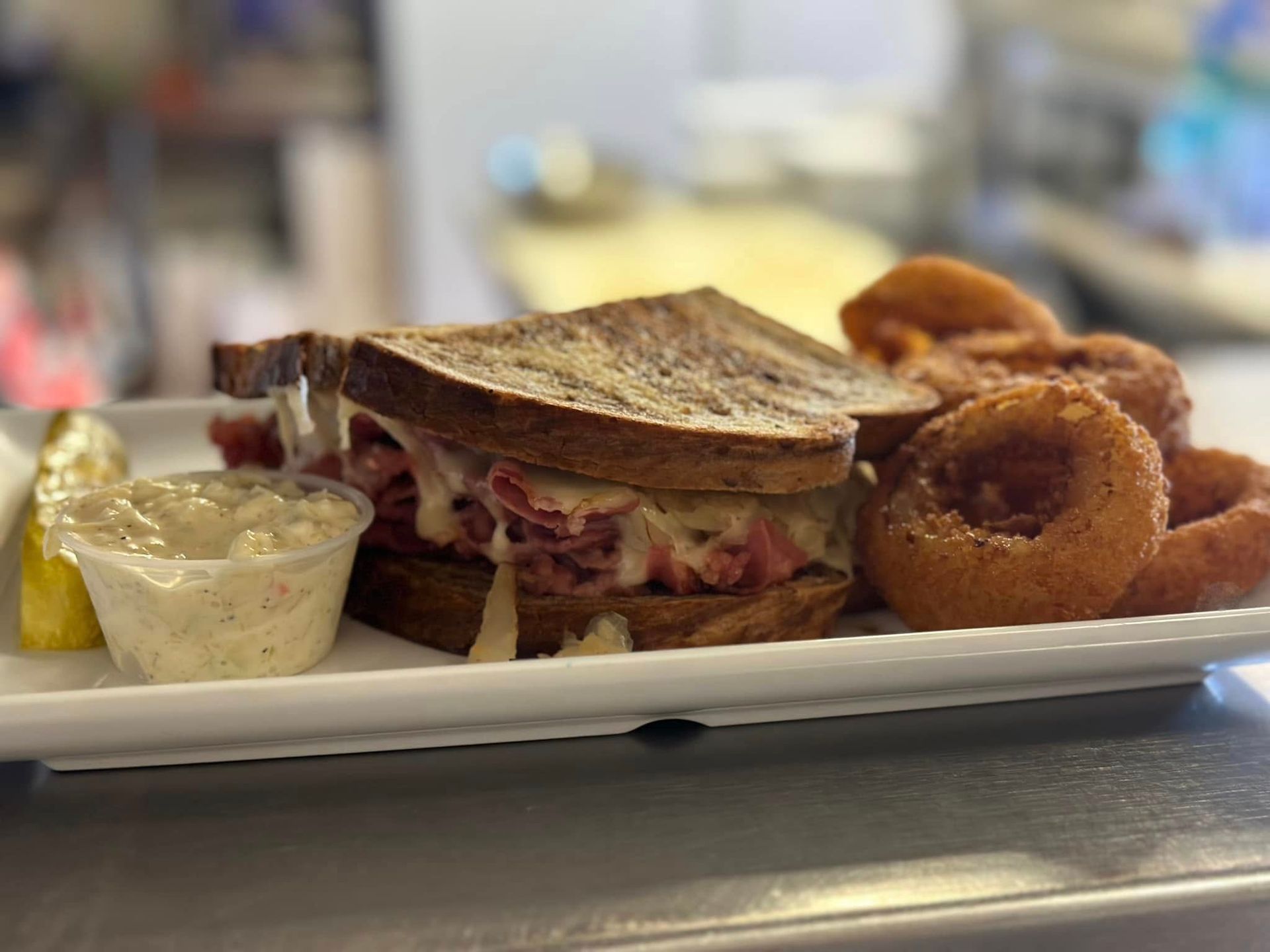 Reuben sandwich with onion rings and coleslaw on a white plate.