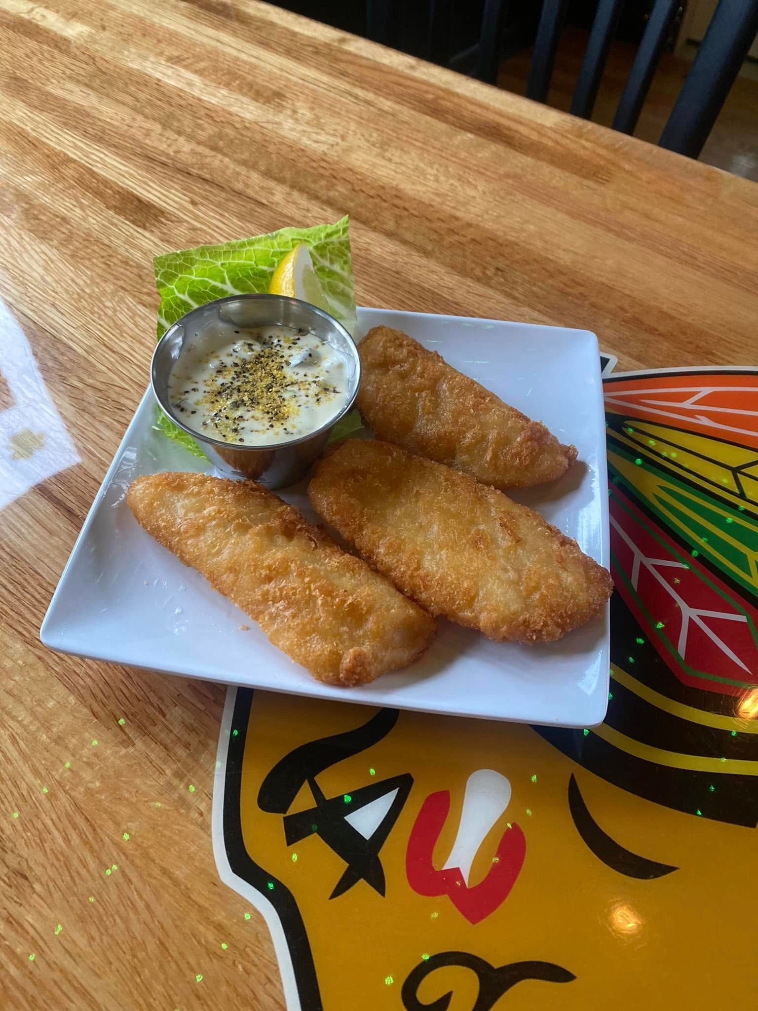 Fried fish fillets, tartar sauce, lemon wedge, on white plate, wooden table.
