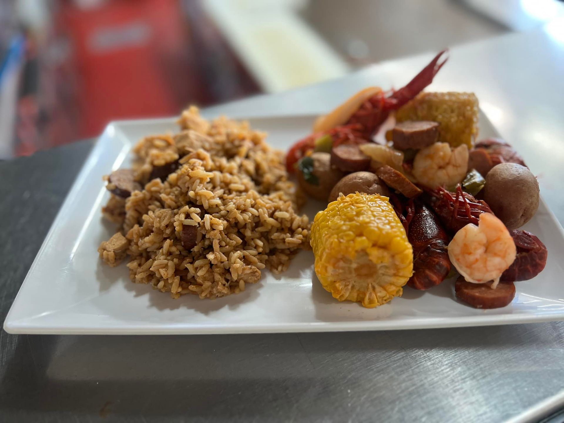 Seafood boil on a white plate: crawfish, corn, potatoes, sausage, shrimp, and fried side.