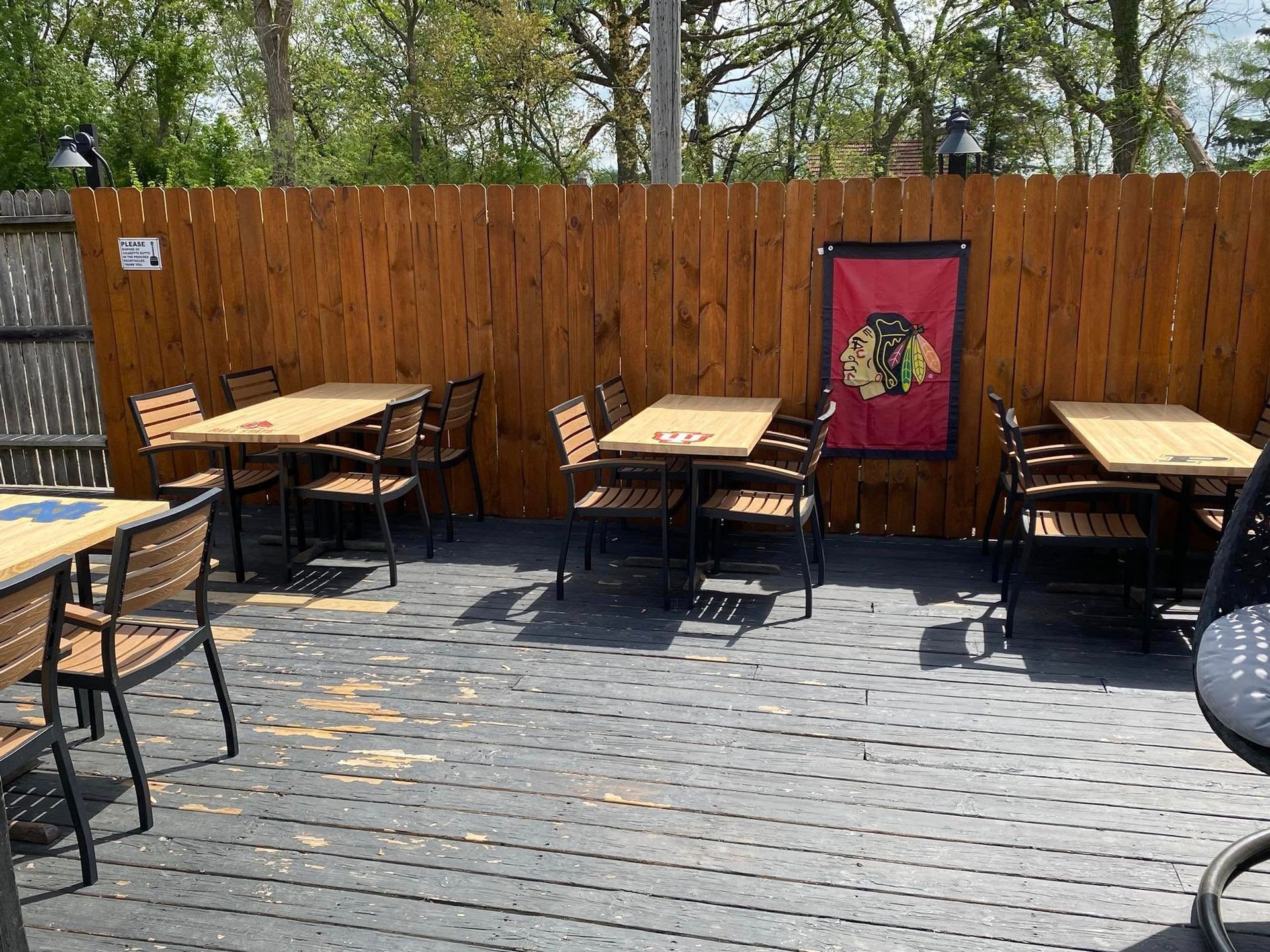 Outdoor patio with wooden tables and chairs, wood fence backdrop, Chicago Blackhawks flag.