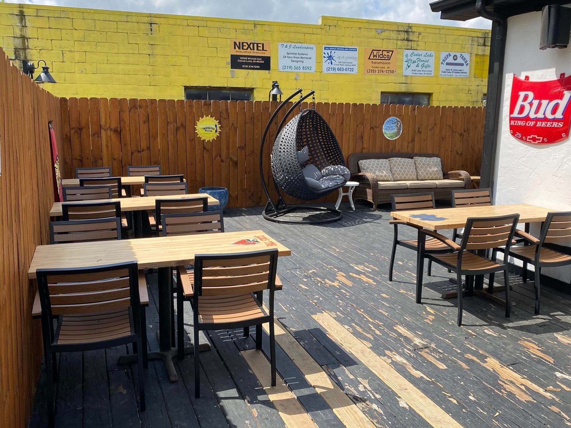 Outdoor patio with tables, chairs, and a hanging chair, against a yellow wall with signage.