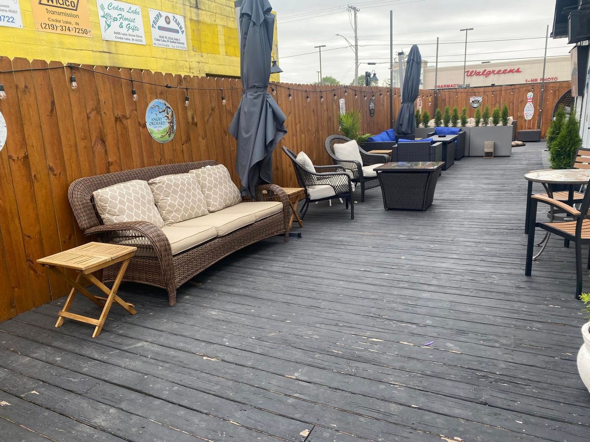Outdoor patio with wicker furniture, wooden deck, umbrellas, and a wooden fence.