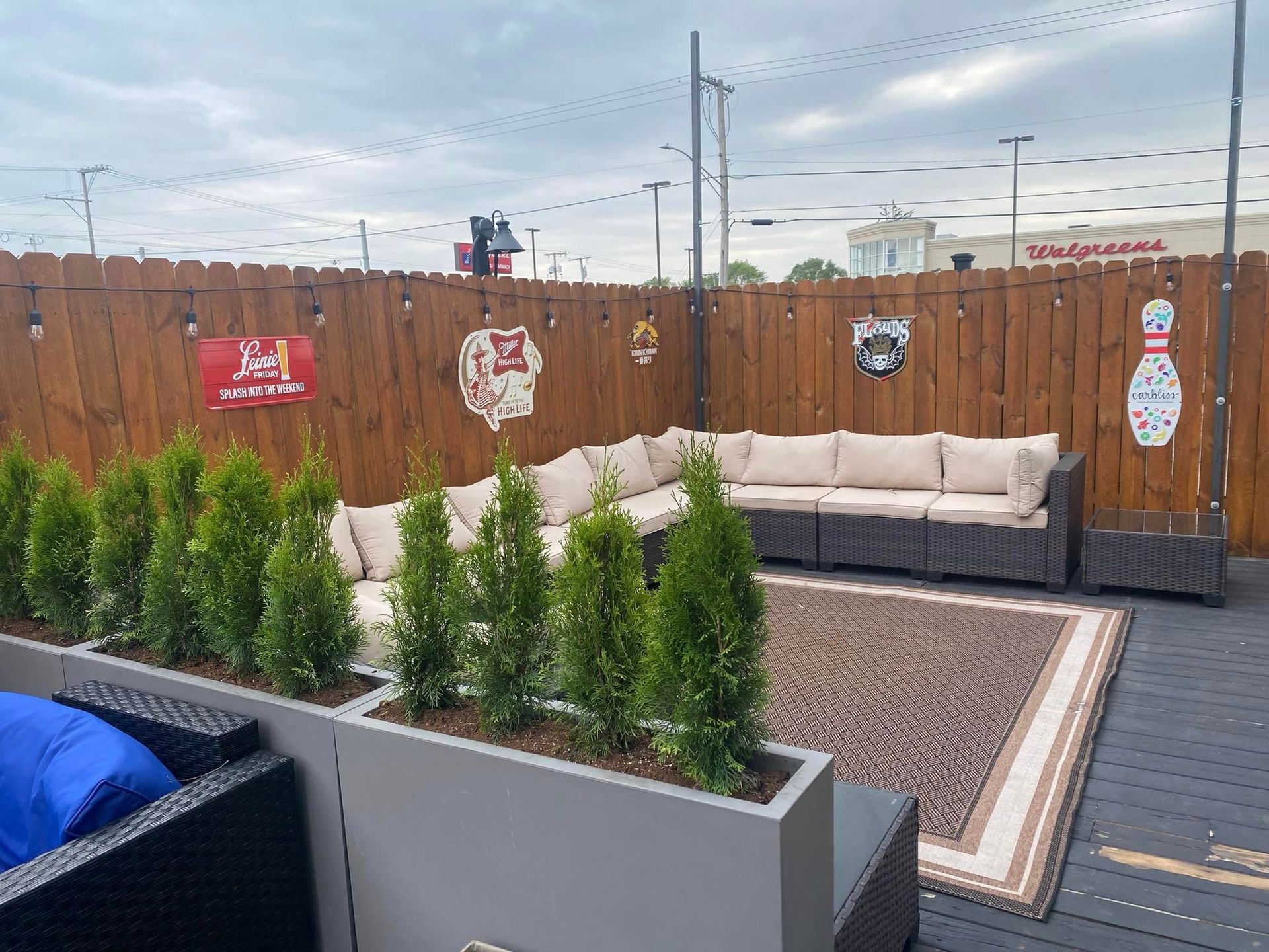 Outdoor patio with couches, wooden fence, greenery, and beer signs.