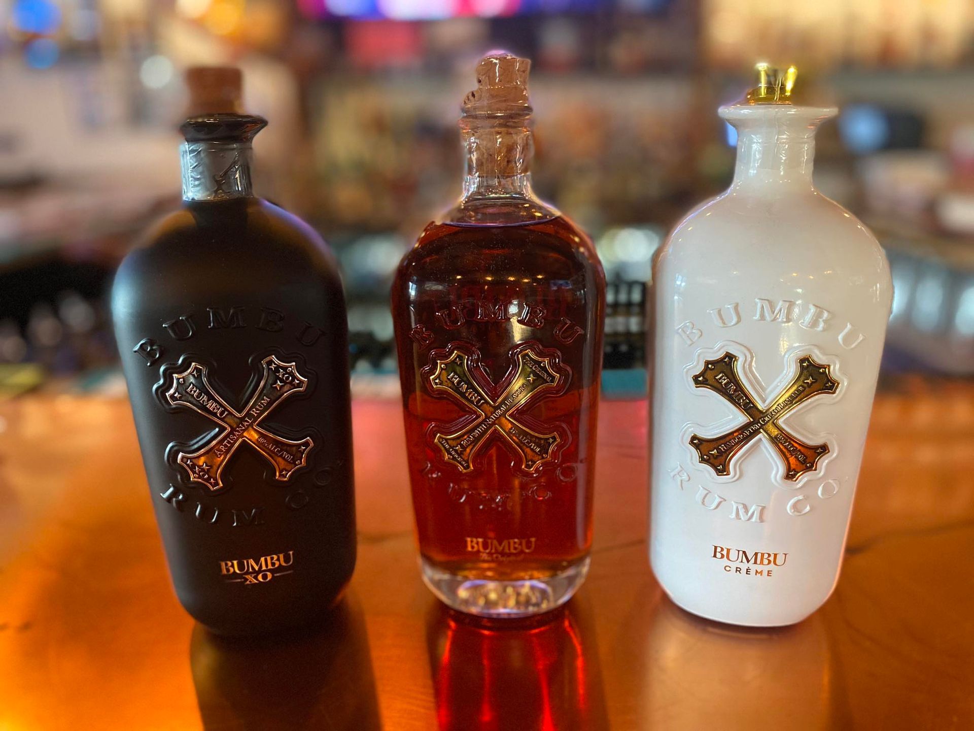 Three rum bottles, black, amber, and white, with skull and crossbones logo.