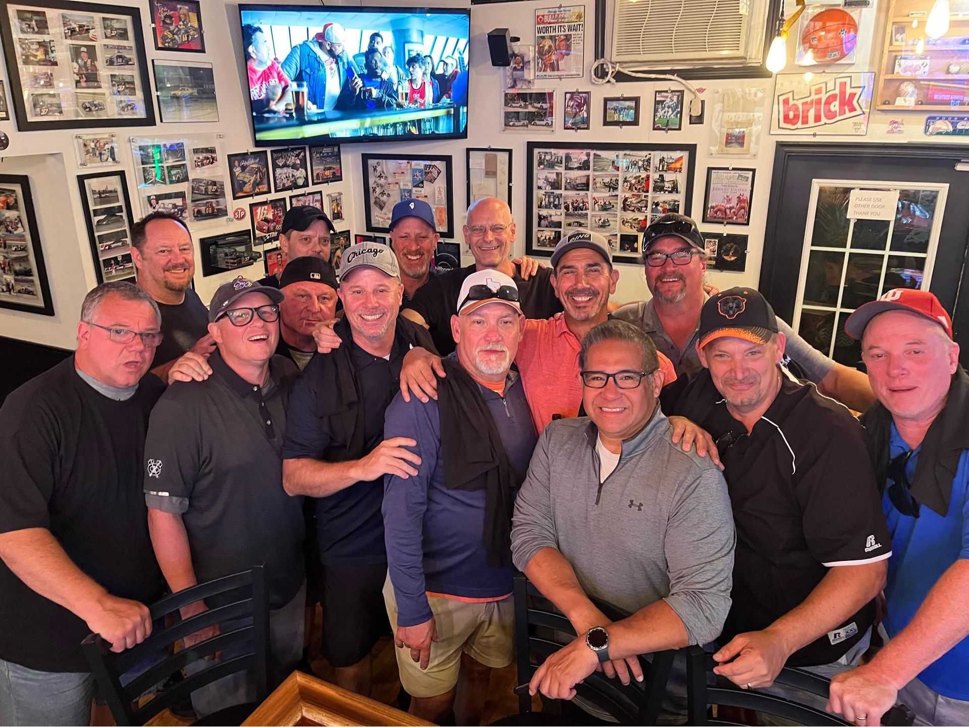Group of men smiling at the camera, inside a bar with memorabilia on the walls.
