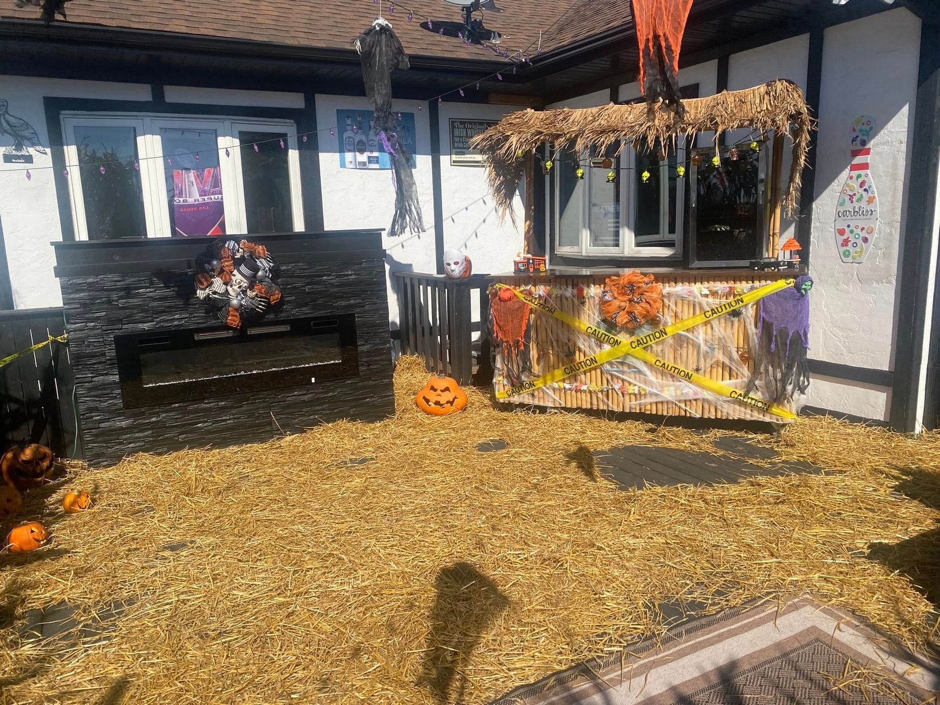 Halloween decorations in a yard; faux fireplace and booth with pumpkins and hay.