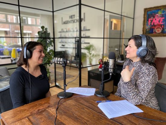 Galit Soesan Shoshanna de Goede Galit en Shoshanna nemen een podcast op aan tafel. De ene gebaart, de andere glimlacht. Microfoons en koptelefoons aanwezig.