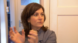 Galit gebaart met haar handen terwijl ze spreekt bij een witte deur, binnen.