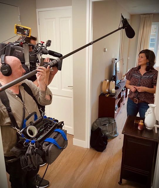 Een filmploeg filmt Galit binnenshuis. Cameraman, geluidstechnicus en Galit staan in de deuropening.