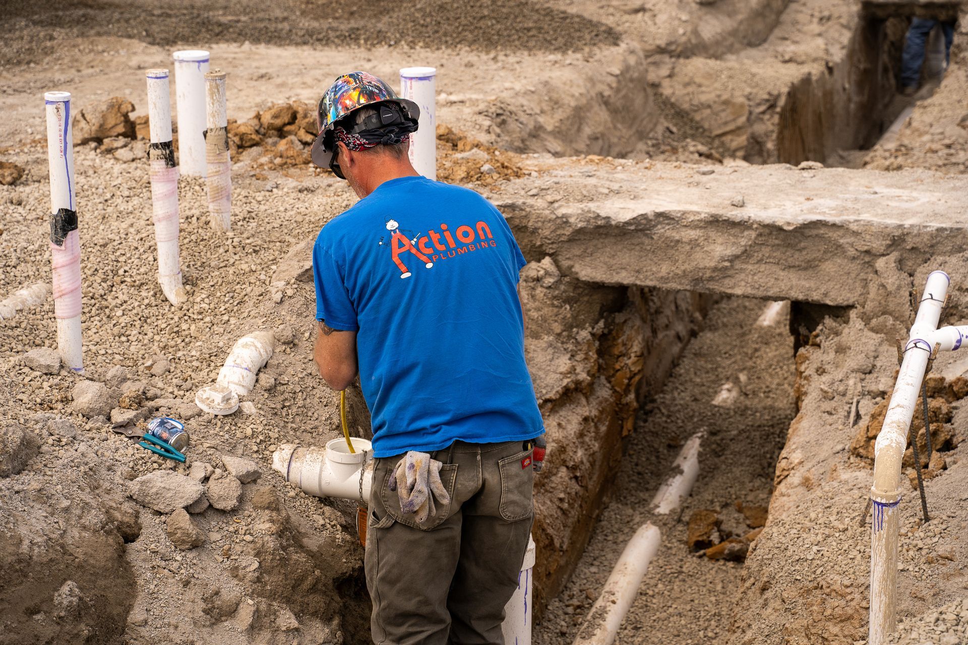 a man in a blue action plumbing shirt is working on pipes .