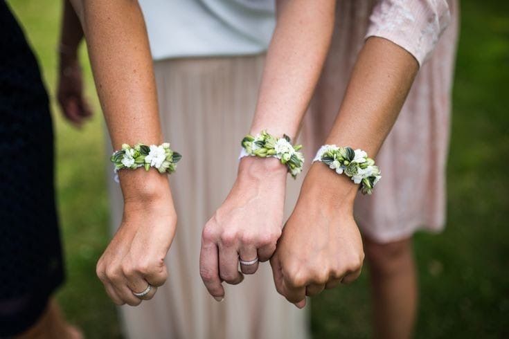 Tre braccia con braccialetti floreali, pugni alzati, probabilmente a un matrimonio.