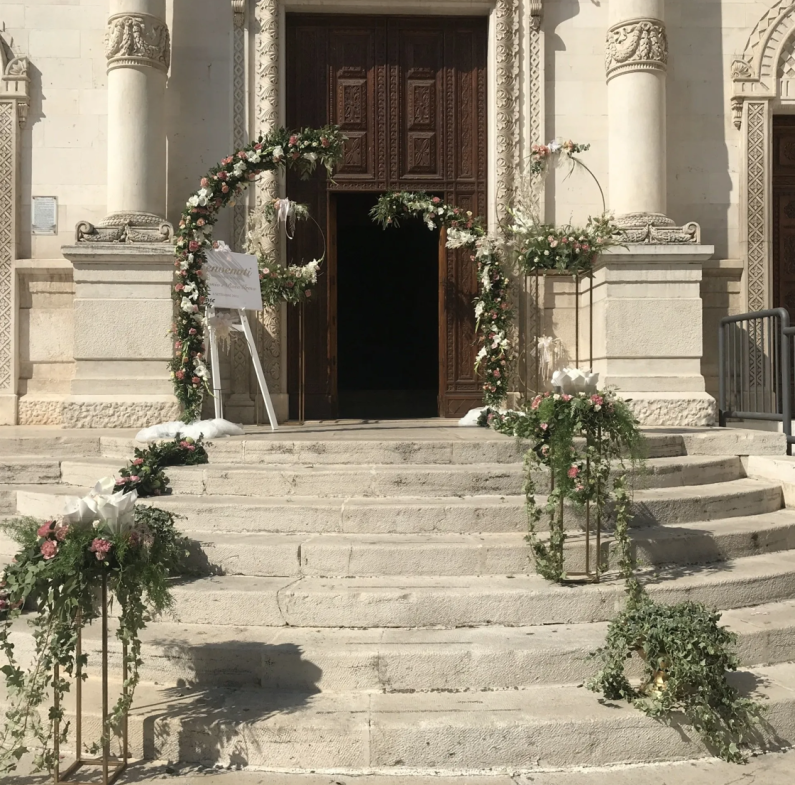 Ingresso della chiesa decorato per un matrimonio con archi floreali e composizioni floreali sui gradini.