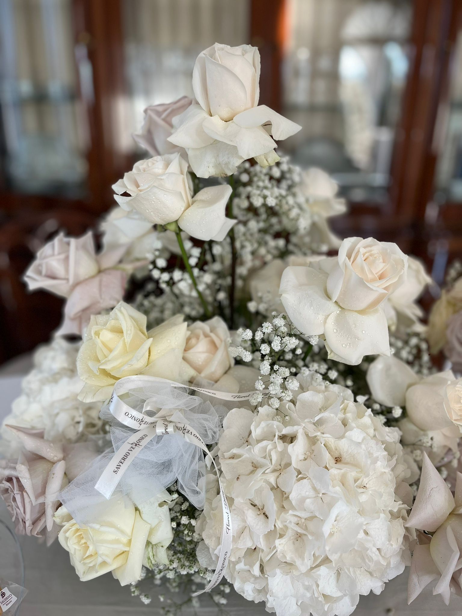 Composizione floreale con rose bianche e ortensie, con decorazioni in gypsophila e nastri.