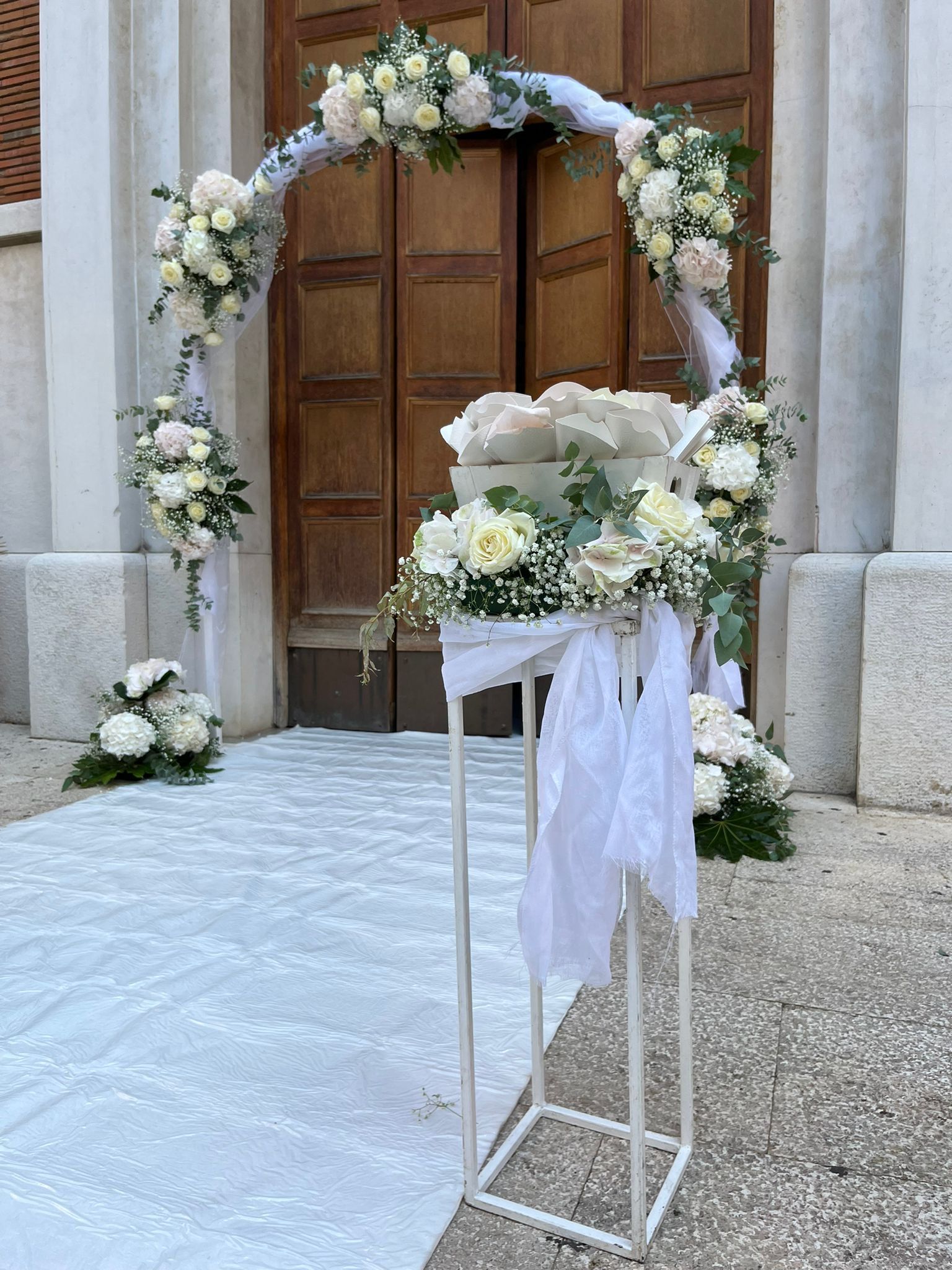 Arco nuziale con fiori bianchi e decorazioni davanti alla porta di una chiesa.