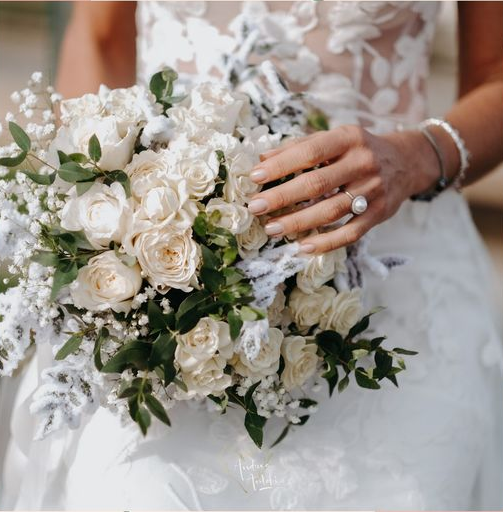 La sposa in abito bianco tiene in mano un bouquet di rose bianche e verde, con l'anello.