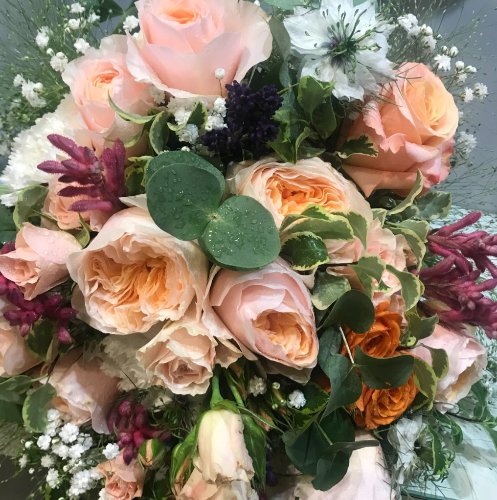 Bouquet di rose color pesca, fogliame verde e fiori bianchi, con accenti viola scuro.