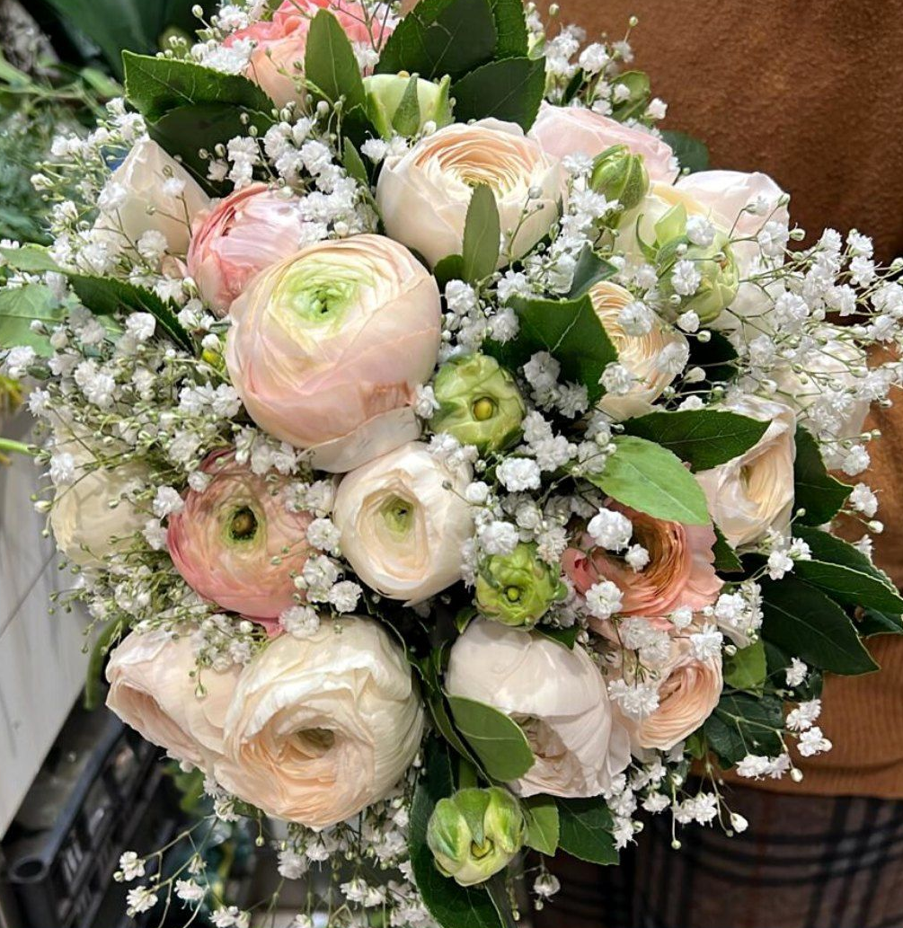 Bouquet di fiori di ranuncolo rosa chiaro e bianchi, gypsophila e fogliame verde.