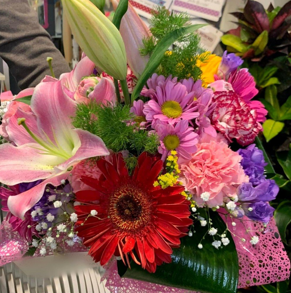 Un bouquet colorato con gerbere rosse, gigli rosa e altri fiori vari in un contenitore bianco.
