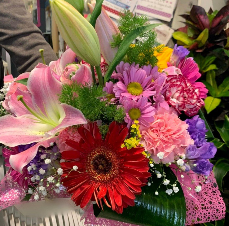 Composizione floreale vivace con gigli rosa, gerbere rosse e vari fiori colorati.