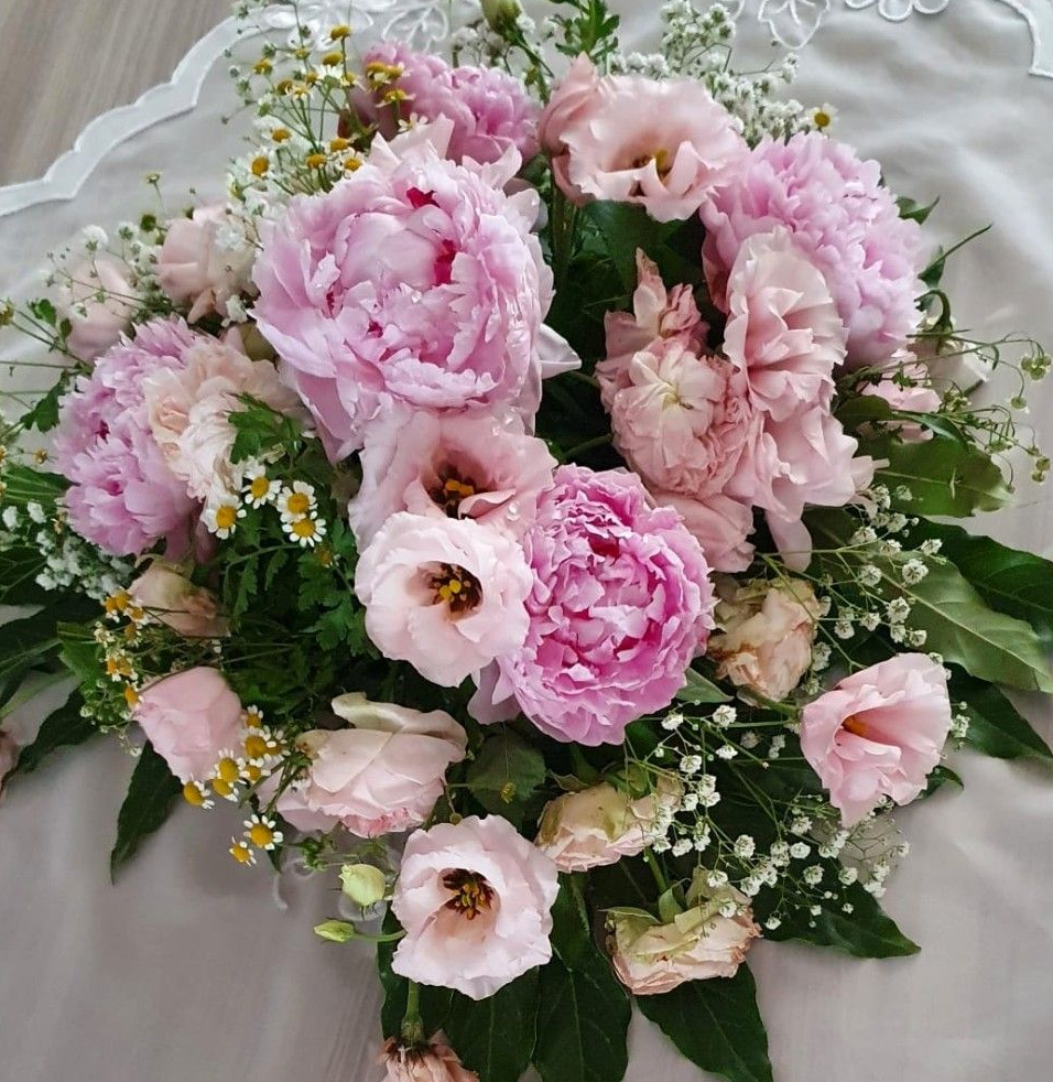 Peonie rosa e fiori di lisianthus con verde, disposti su tessuto.