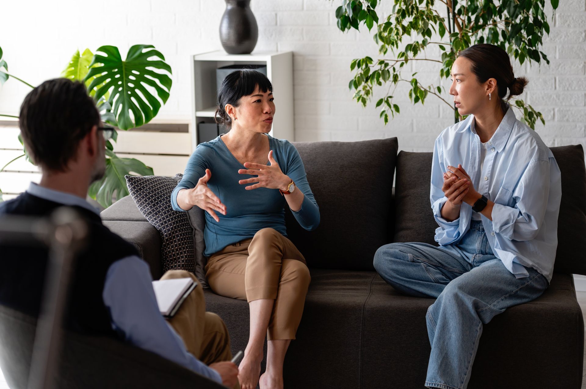 Three people in a living room discussing with a coach, seated on a sofa and chair.