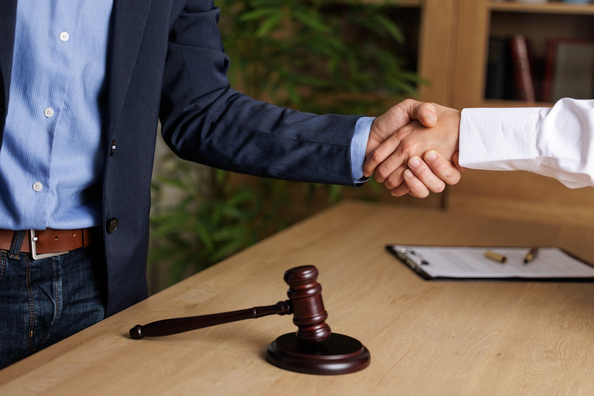 Two people shake hands across a desk with a gavel in the foreground.