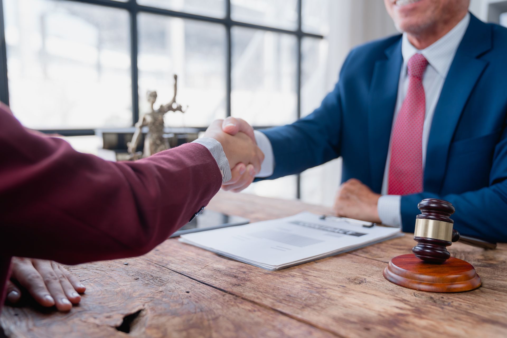Business handshake across a wooden table with contract papers and a gavel in an office