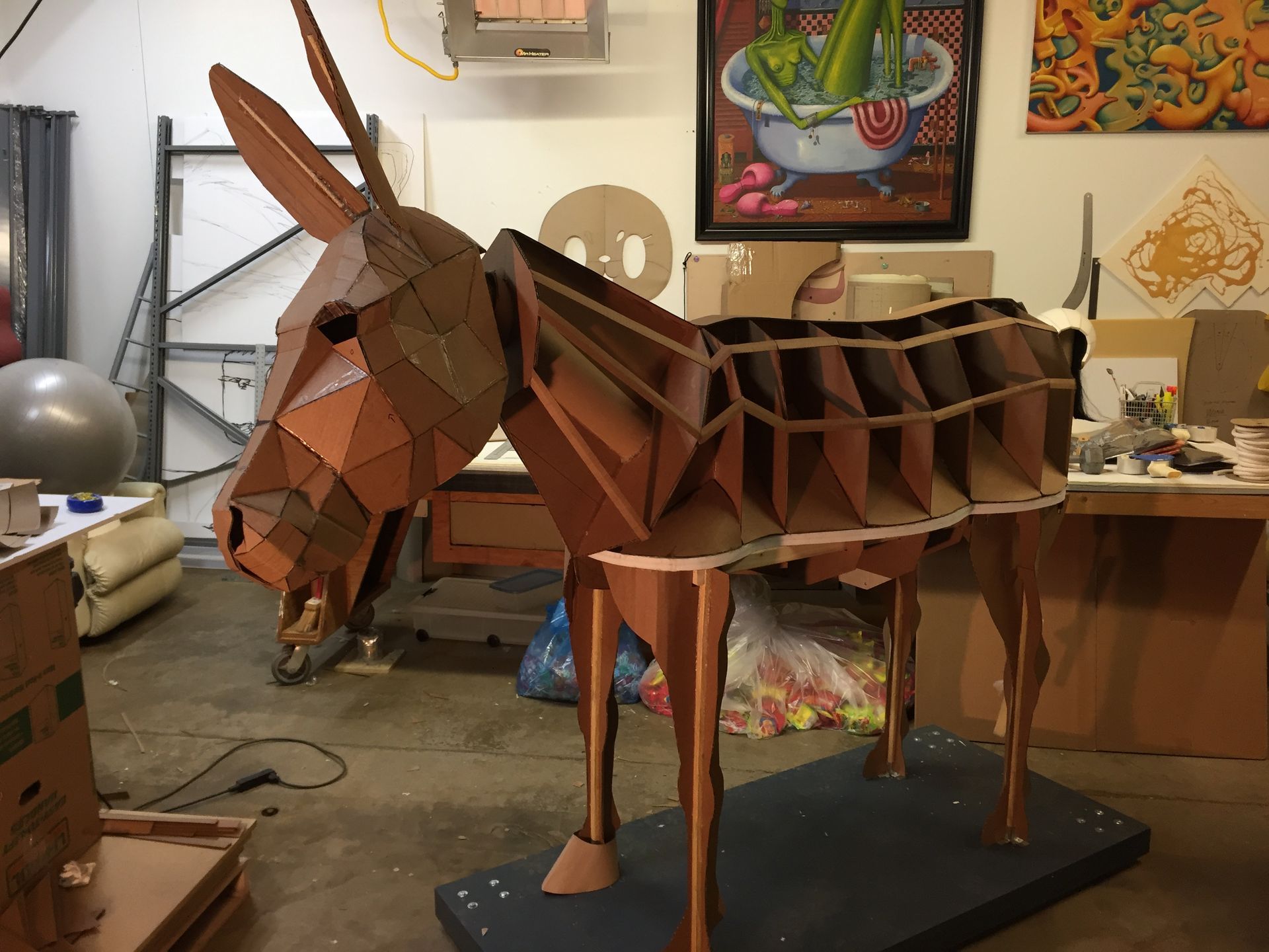 A large, brown, geometric donkey sculpture in a workshop.