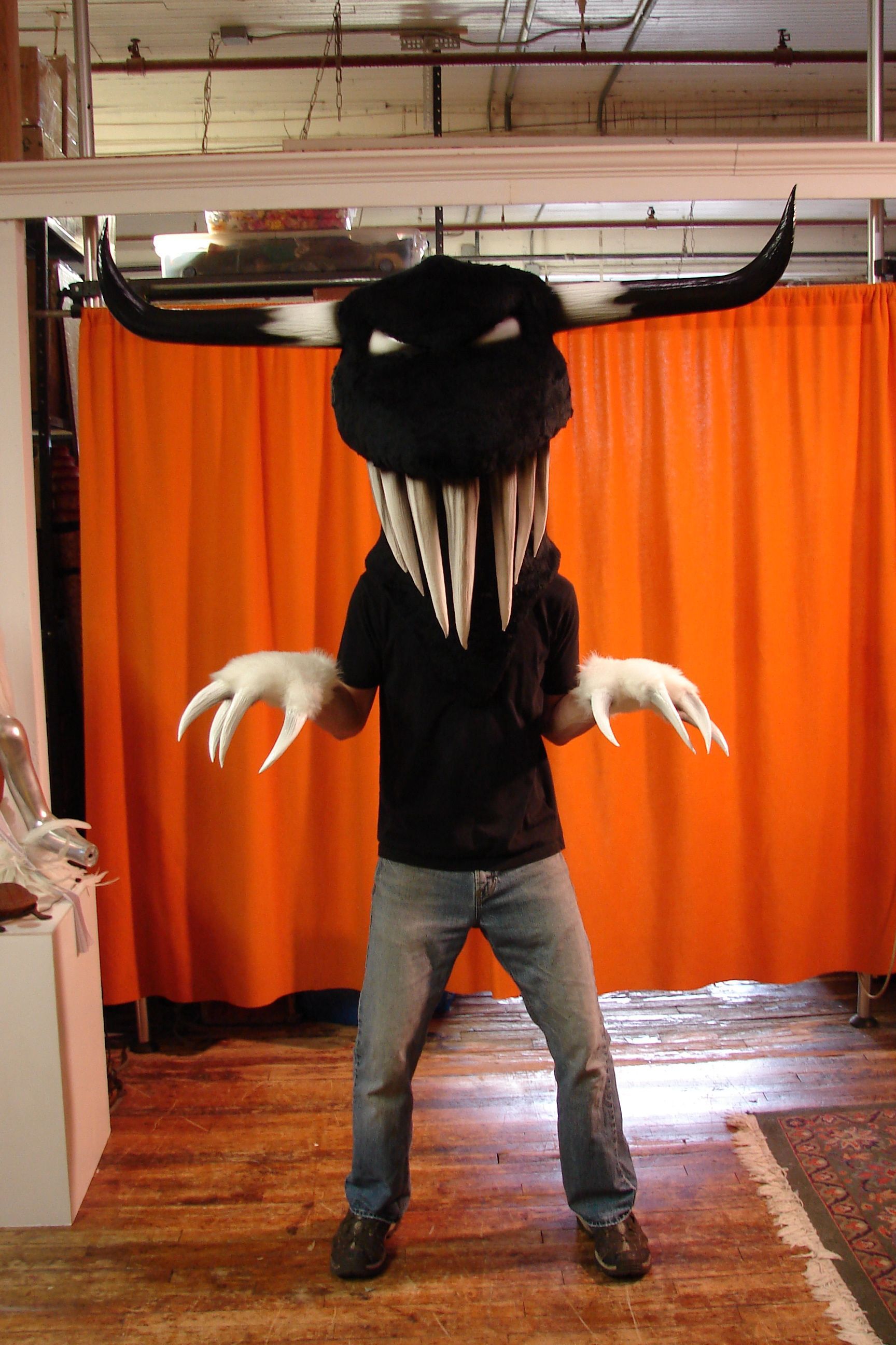 A man in a monster costume is standing in front of an orange curtain.