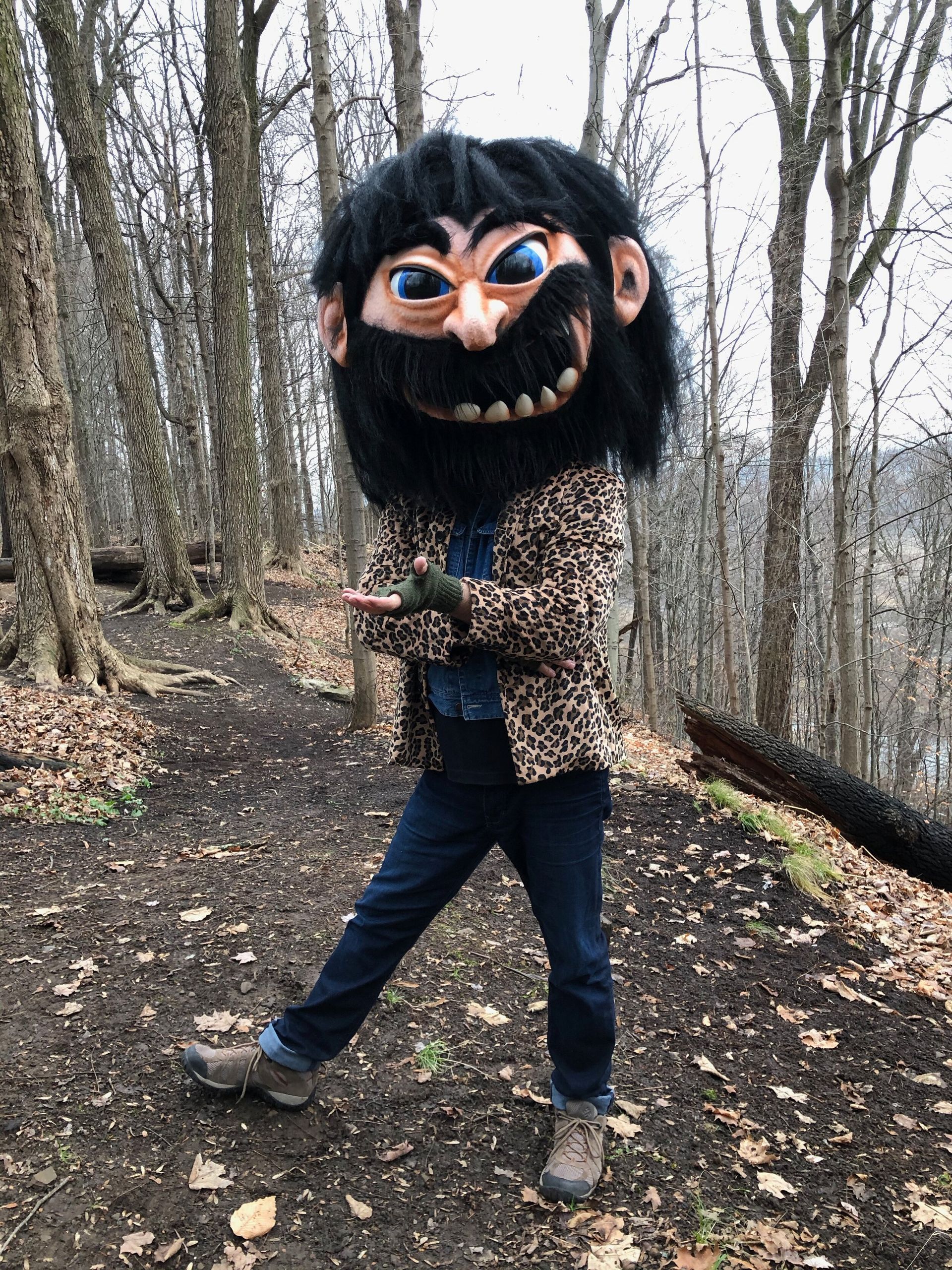 A man in a leopard print jacket and a bearded mask is standing in the woods.