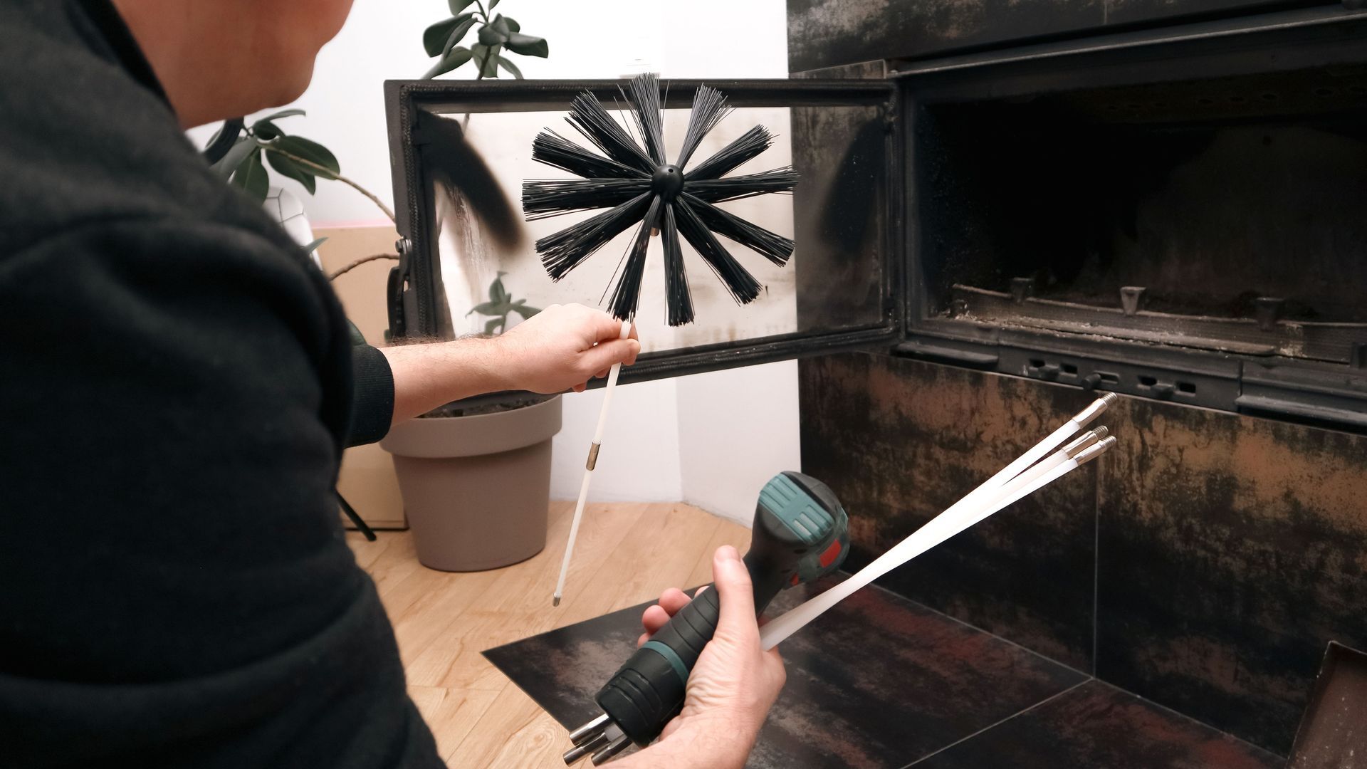 Person cleaning a fireplace chimney with rotary brushes and maintenance tools indoors.