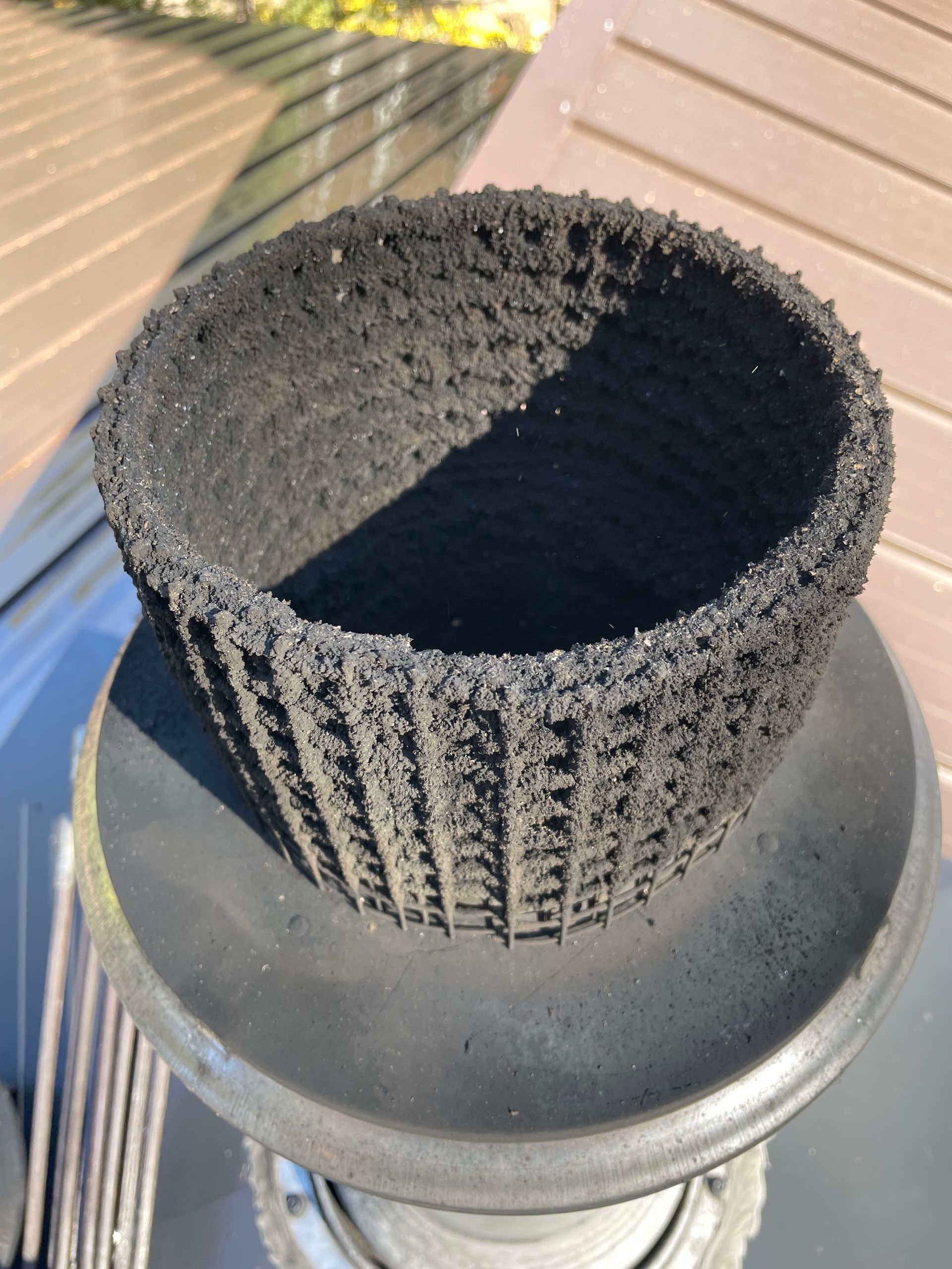 Black, soot-covered mesh cap of a chimney. Outdoors on a sunny day.
