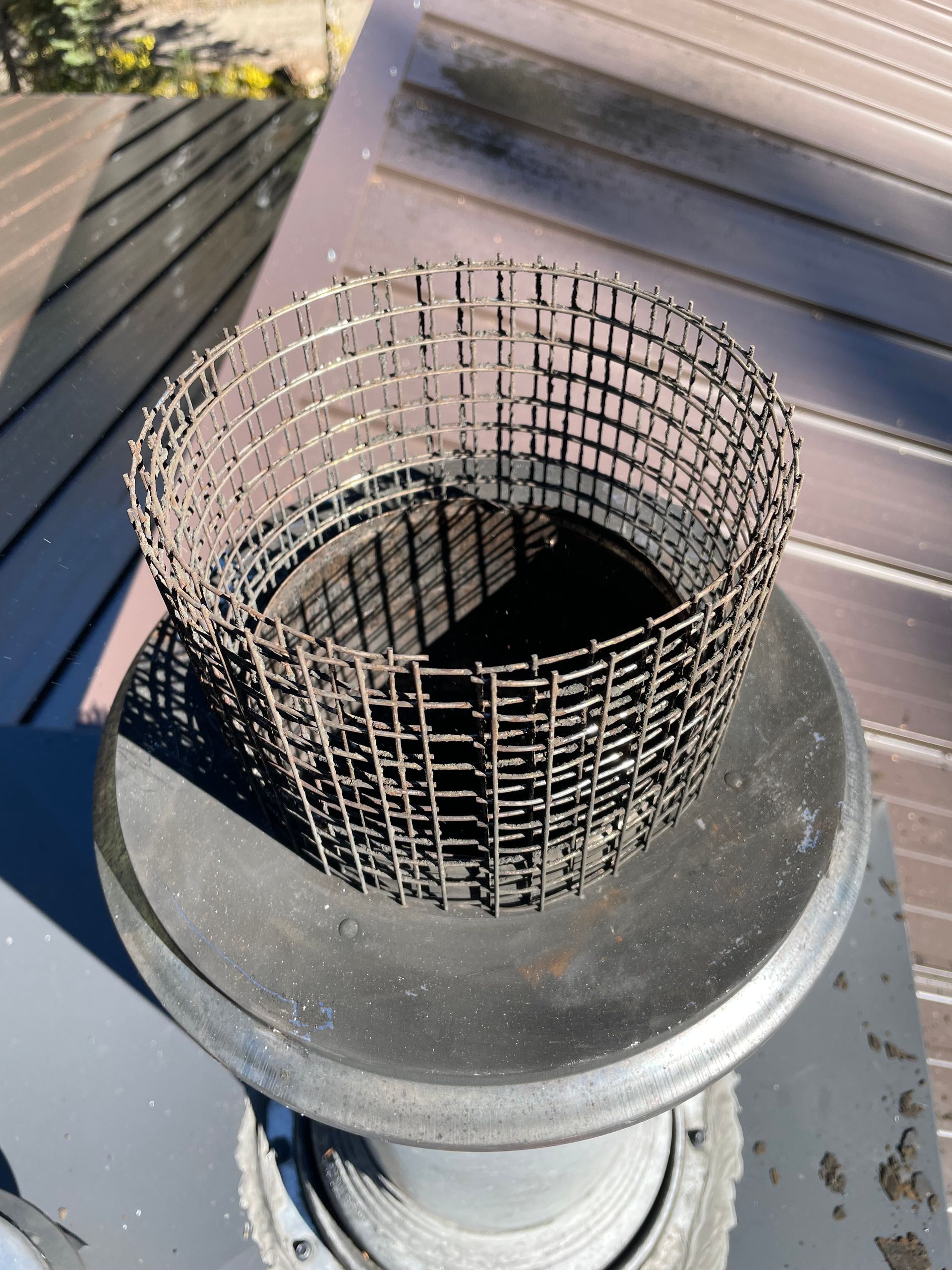 Metal mesh chimney cap on a gray pipe, on a dark brown roof.