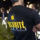 Vue de dos d'un agent de sécurité portant une chemise noire avec l'inscription et le logo « SECURITE » en jaune. Foule en arrière-plan.