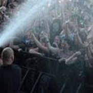 Foule de concert les bras levés ; lumières de scène allumées ; agent de sécurité à la barrière.