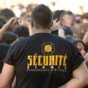 Agent de sécurité en t-shirt noir à inscription dorée, face à la foule.