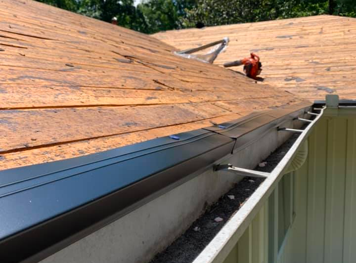 A roof with shingles being removed and a gutter being installed.