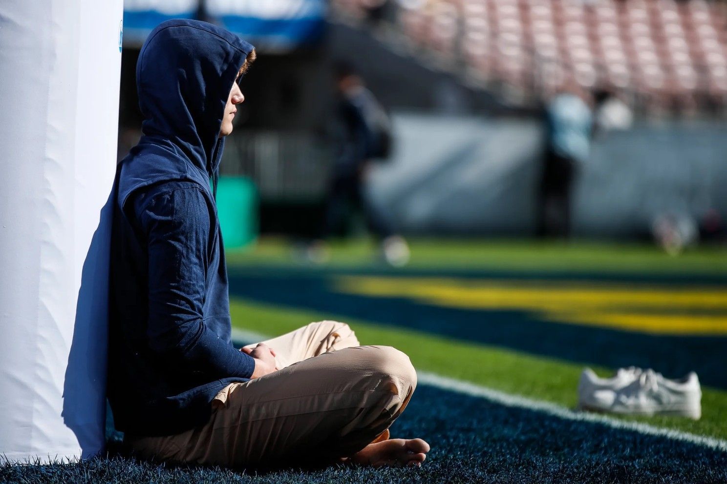 A man in a hoodie is sitting on a football field.