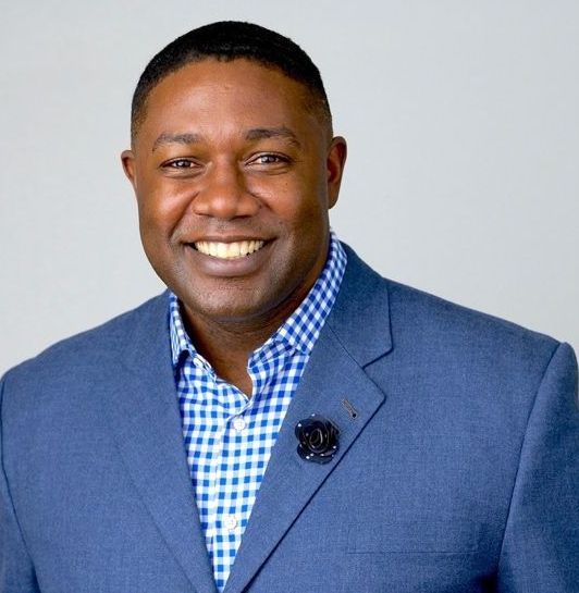 A man in a blue suit and plaid shirt is smiling for the camera