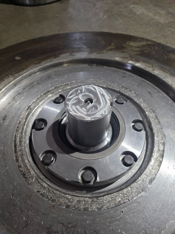 Silver metal part with bolts, center cylinder with spiral grooves, set in a larger circular metal.