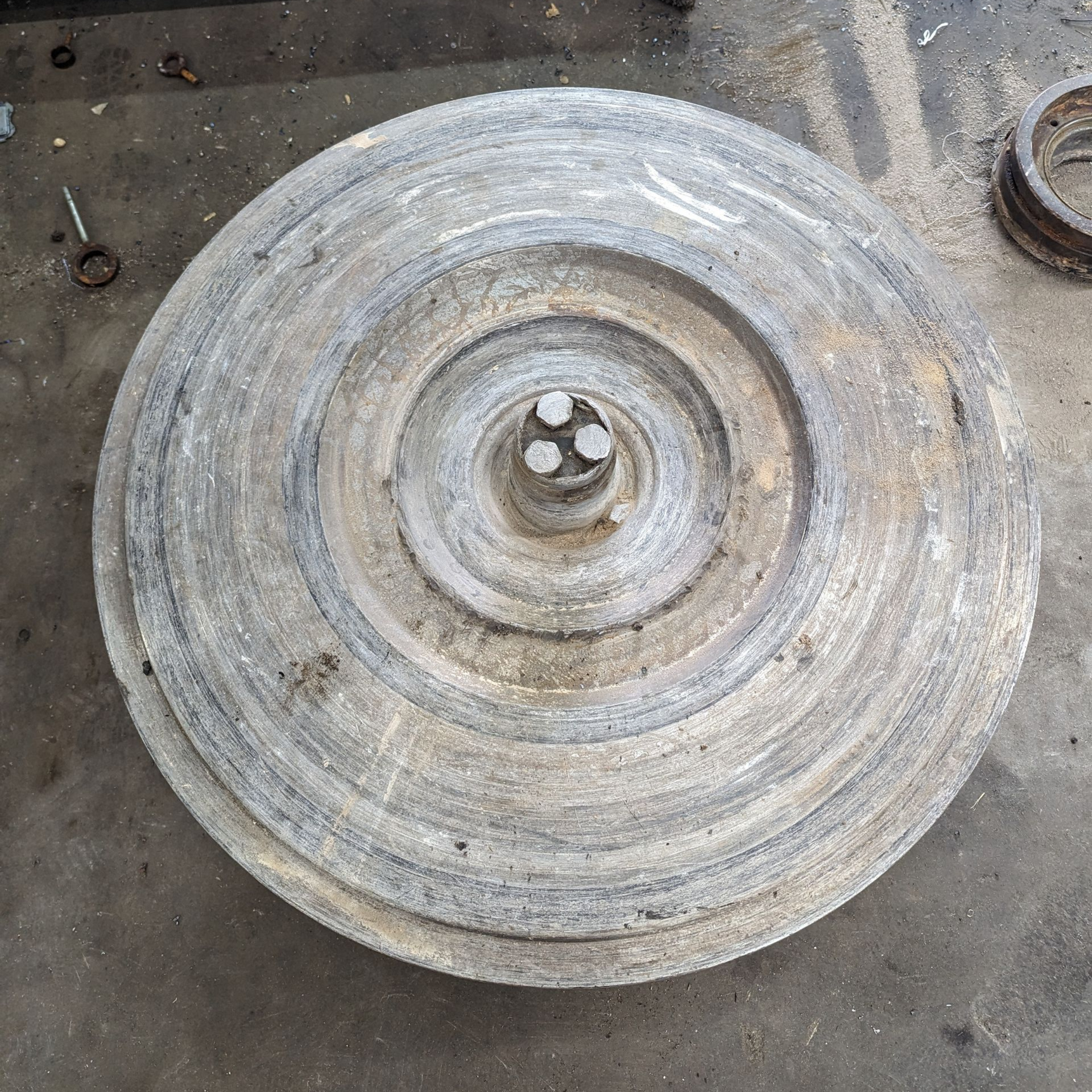 Large, circular, weathered metal wheel with a central hub, sitting on a concrete surface.