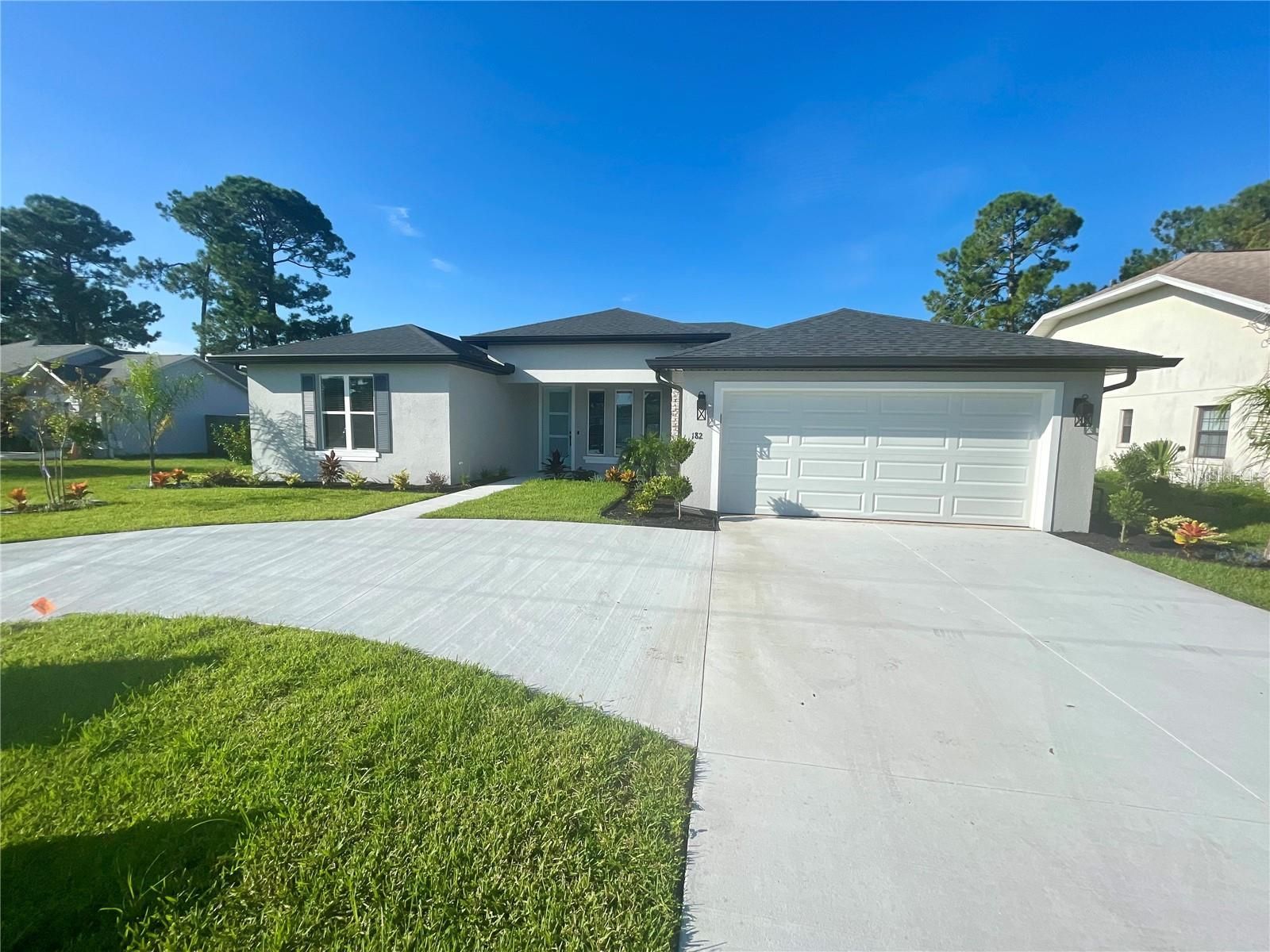 A one-story light gray house with a concrete driveway and green lawn under a blue sky.