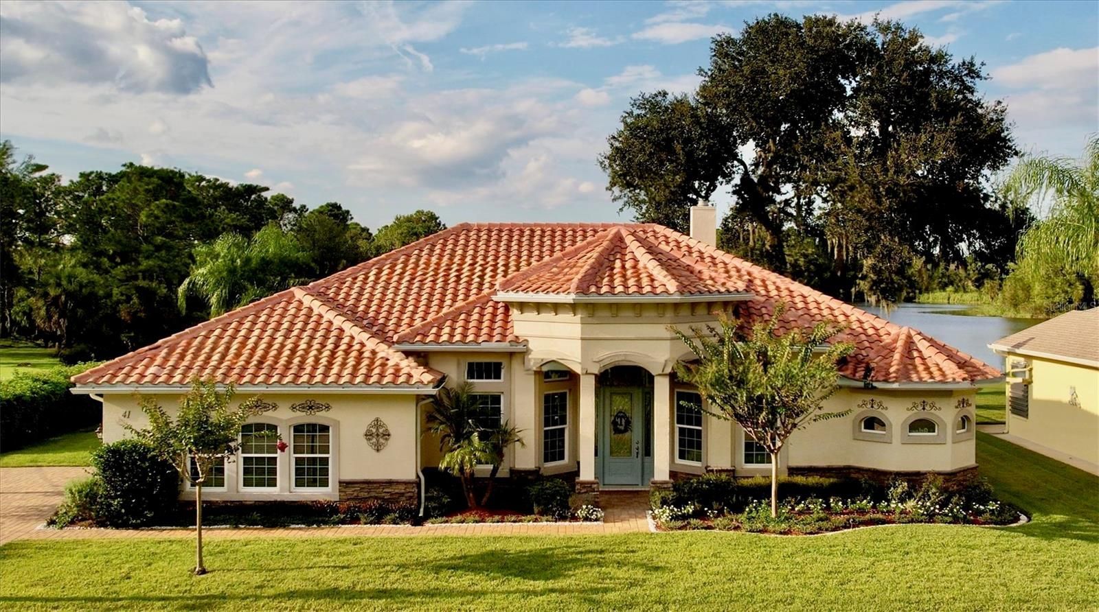 Beige house with orange tiled roof, green lawn, and lake in background.