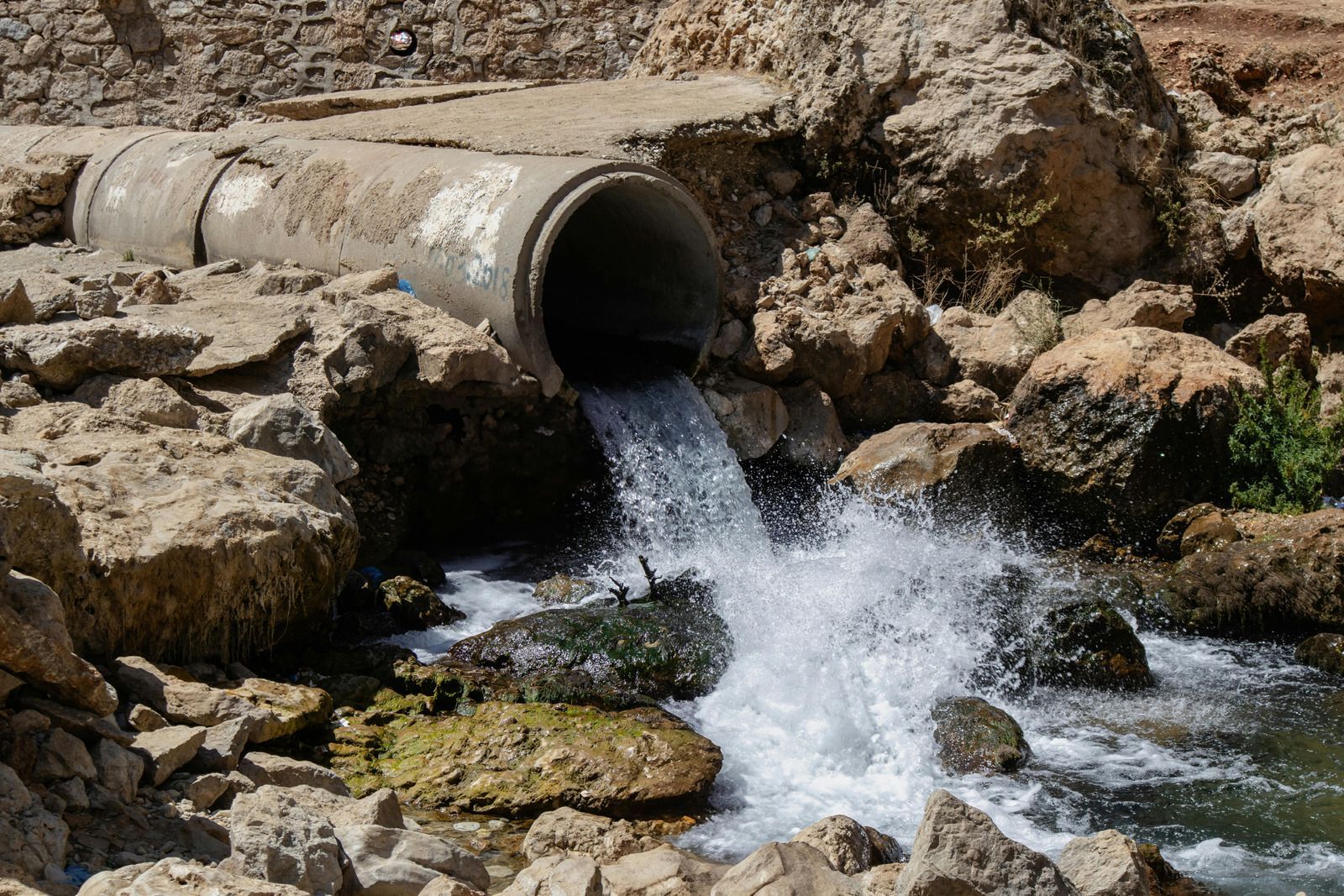 A concrete pipe discharging water into a rocky area.