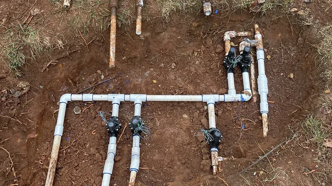 Overhead view of buried irrigation system: PVC pipes, valves, and connections in brown soil.