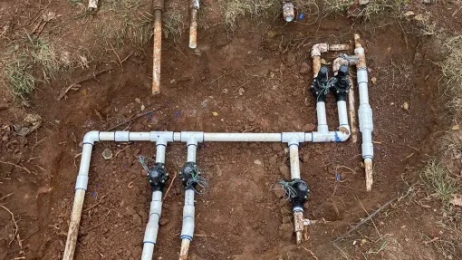 Damaged blue pipe spraying water in an excavated area near a concrete pipe.