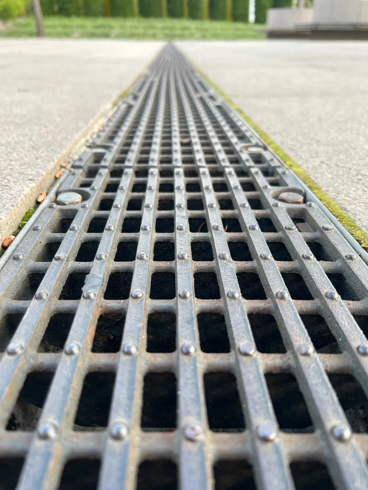 Metal drainage grate embedded in concrete pathway, leading into the distance.