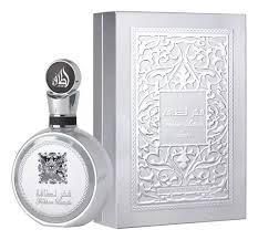Frasco de perfume plateado junto a una caja de embalaje plateada repujada sobre un fondo blanco.