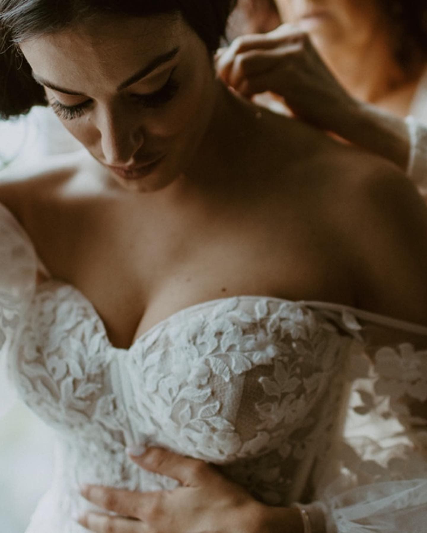 Woman adjusting a white lace wedding dress with off-shoulder sleeves, looking down